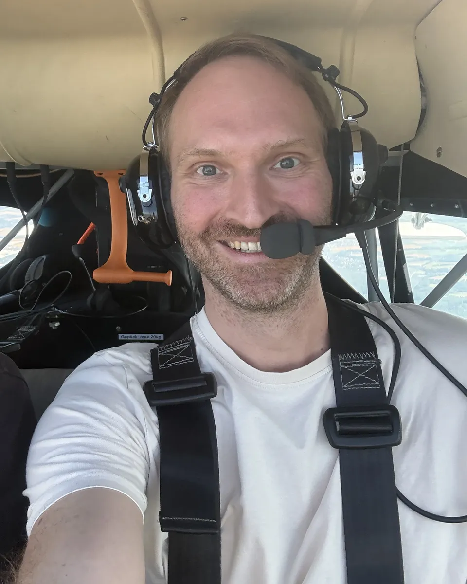 André Gensler mit Headset im Cockpit, hinter ihm die Landschaft aus der Luft